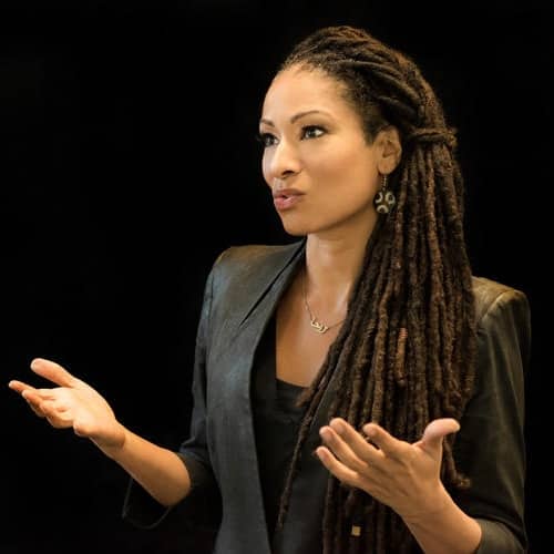 Ruha stands presenting gesturing with open hands