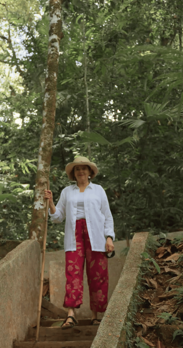 Alane Freund walking on a jungle path at the Imiloa eco resort in Costa Rica (wearing sun hat and linen, holding a bamboo walking stick.)