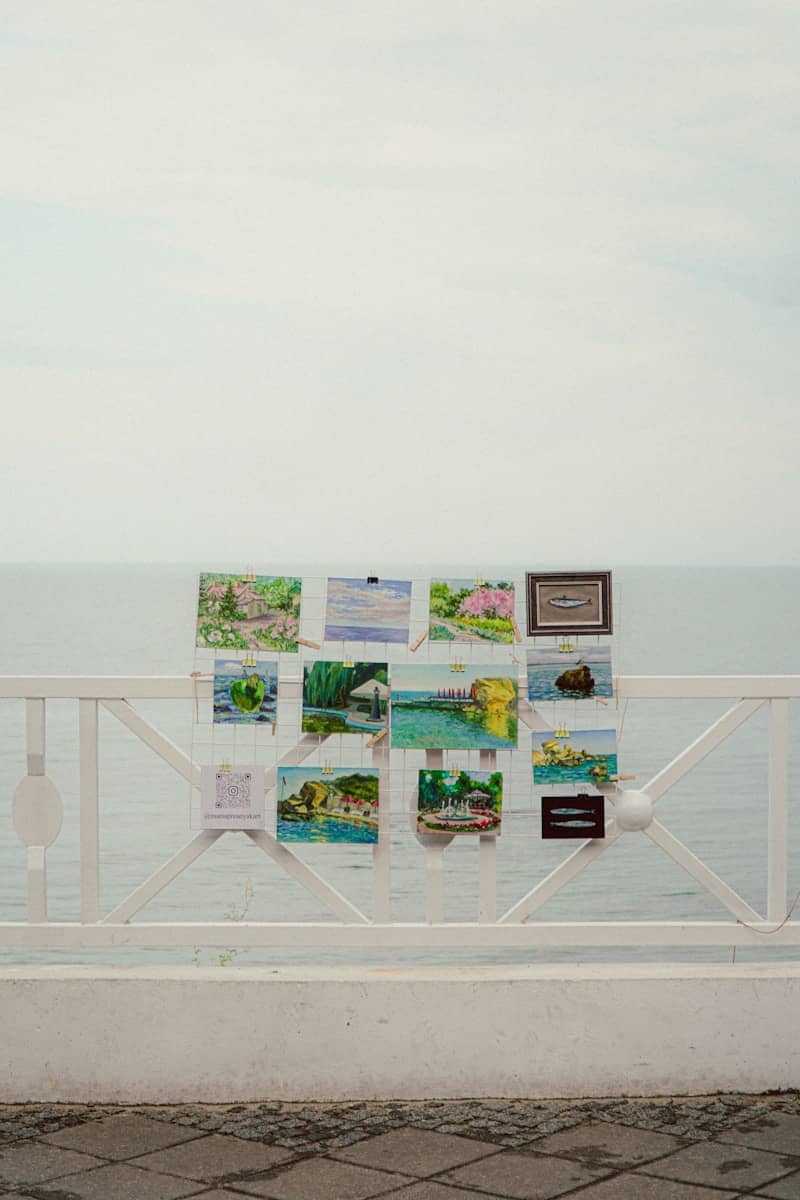 Paintings are displayed on a balcony overlooking the ocean.