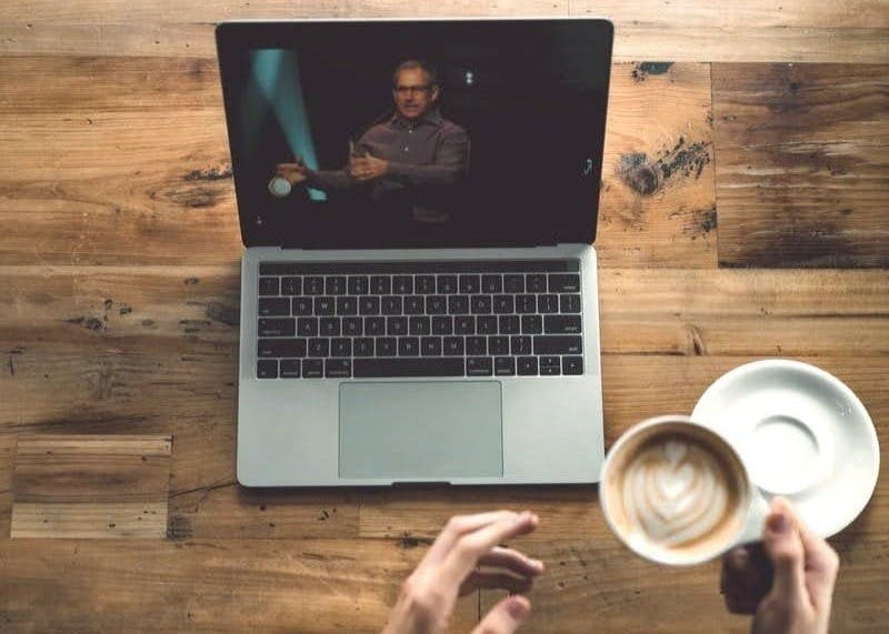 person holding cup of latte while facing MacBook Pro