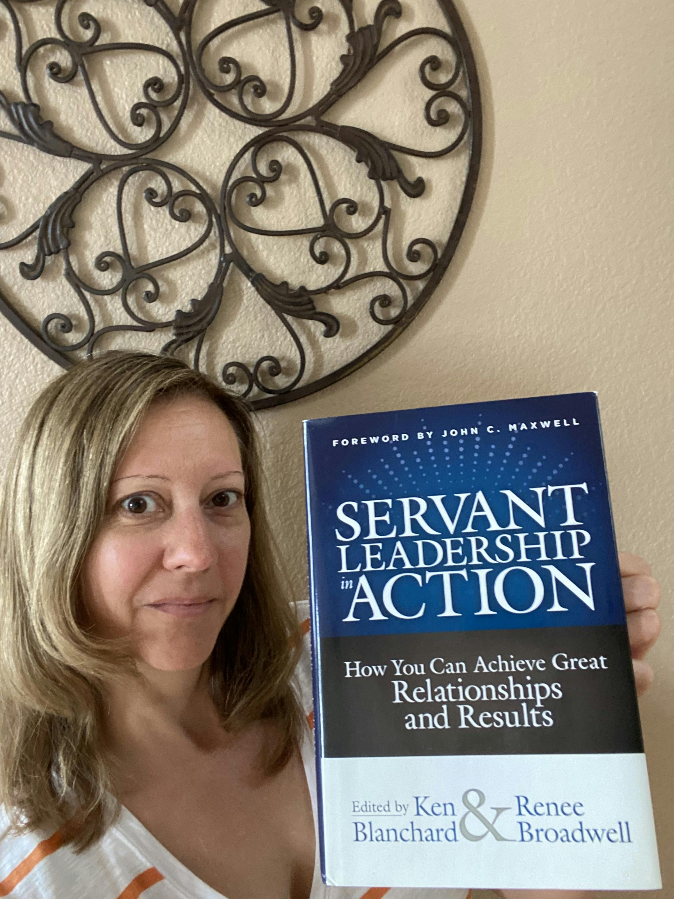 Stephanie holding up the book "Servant Leadership in Action" edited by Ken Blanchard & Renee Broadwell 