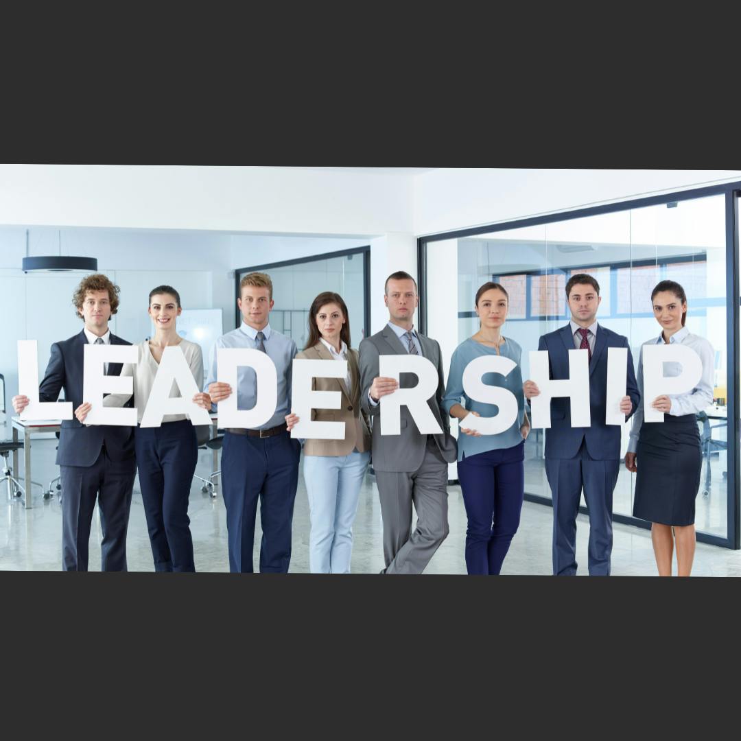 Both male & female corporate leaders in an office setting standing side by side. They each hold up a giant letter, spelling out the word "LEADERSHIP".