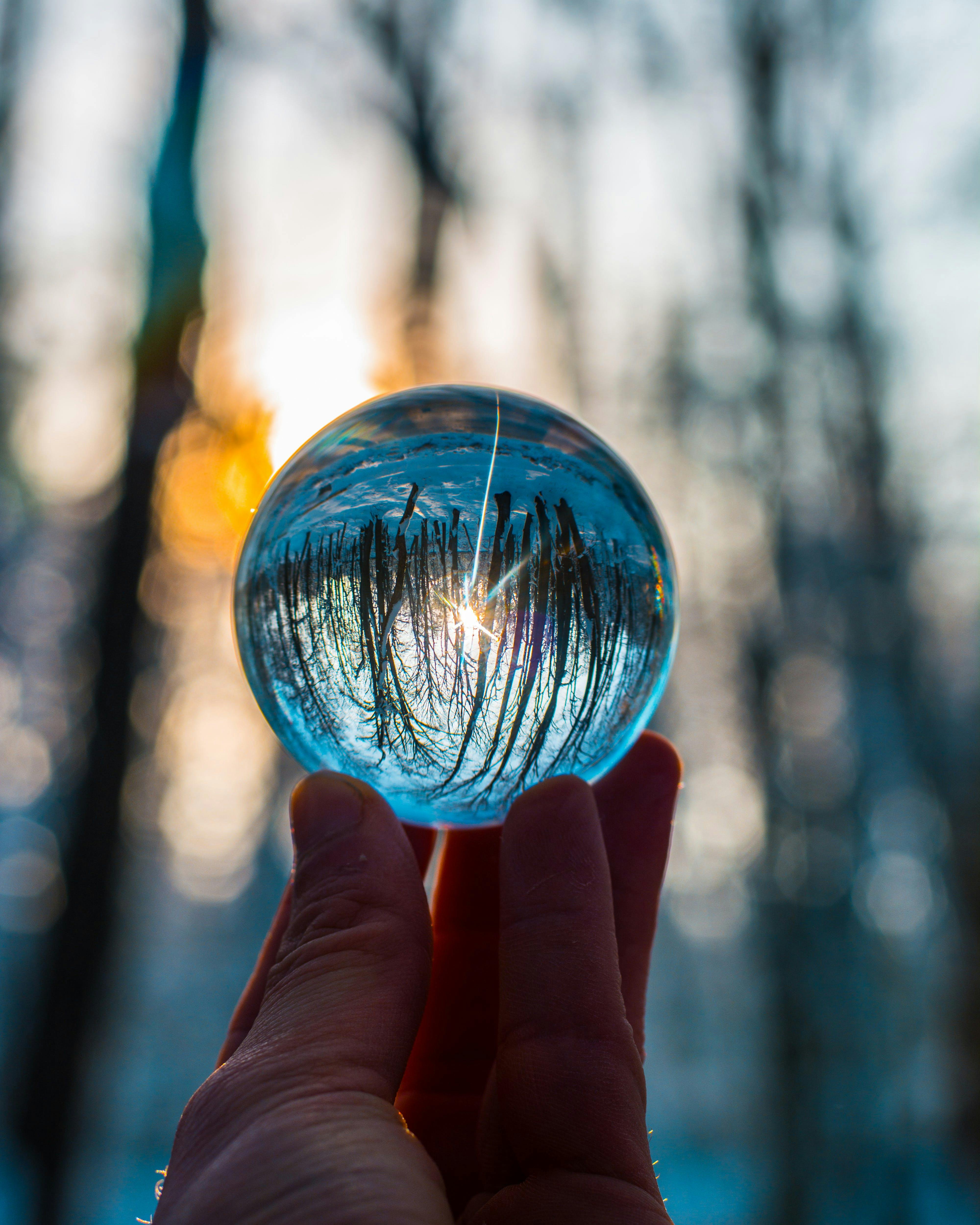 A person's hand holding a glass sphere that is reflecting the surroundings back, but upside down. 