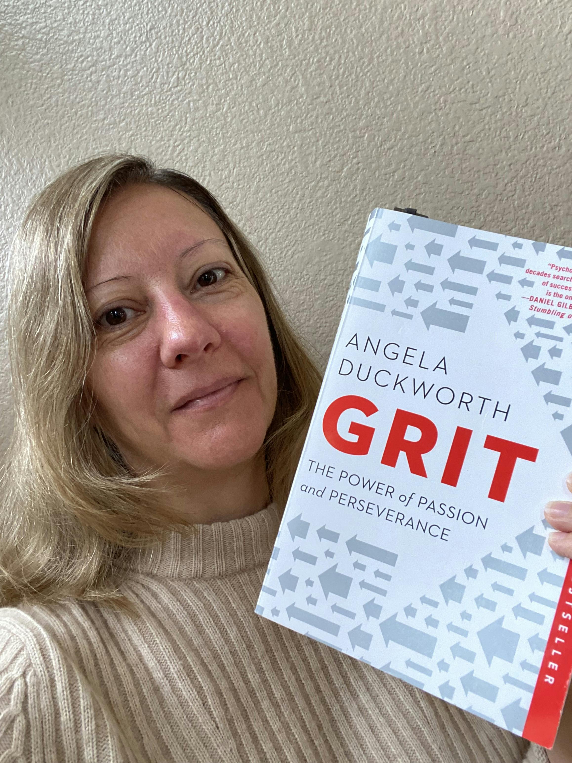 A photo of Stephanie holding up the book 'Grit' by Angela Duckworth. 