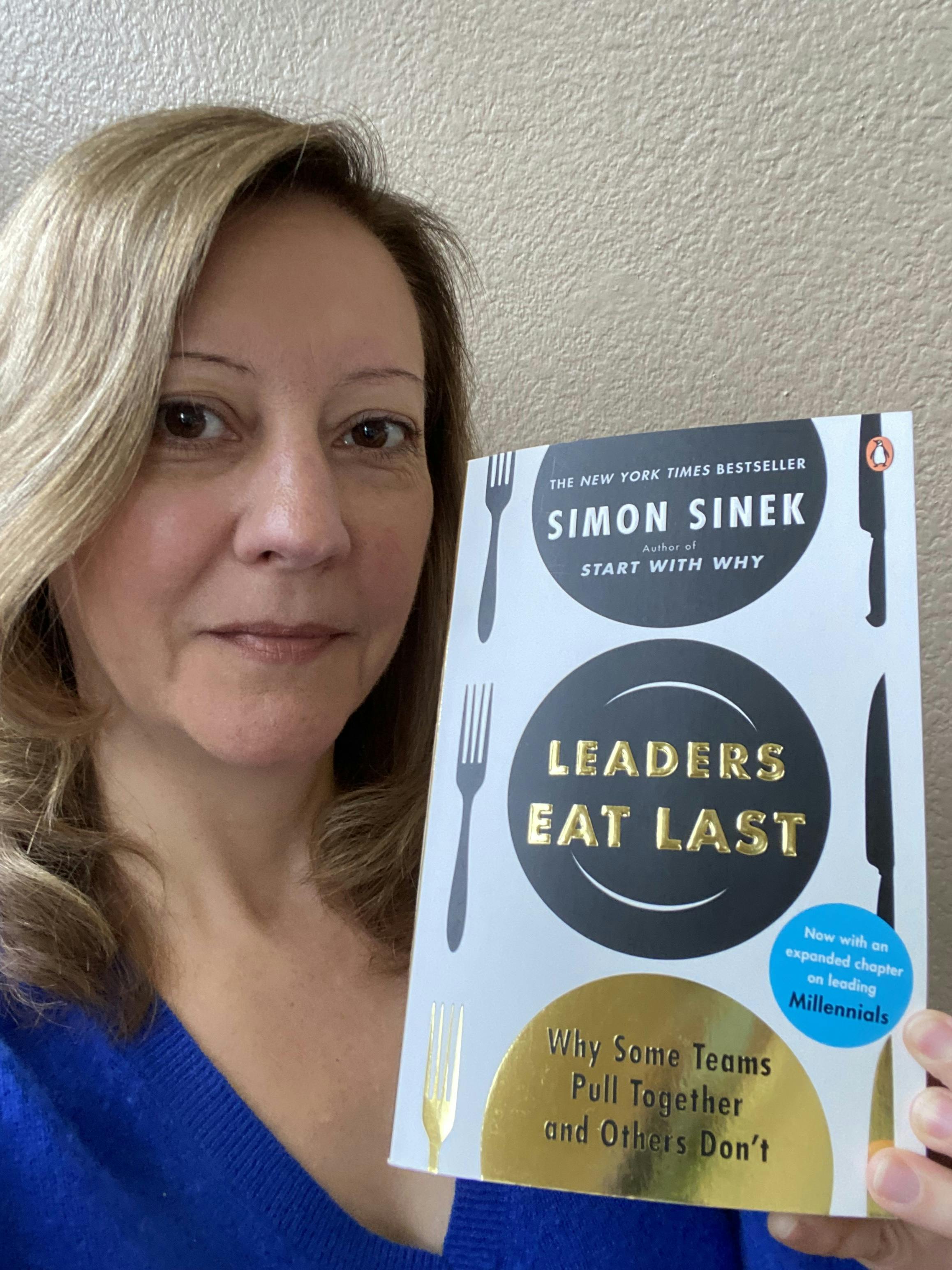 A photo of Stephanie holding the book "Leaders Eat Last" by Simon Sinek 