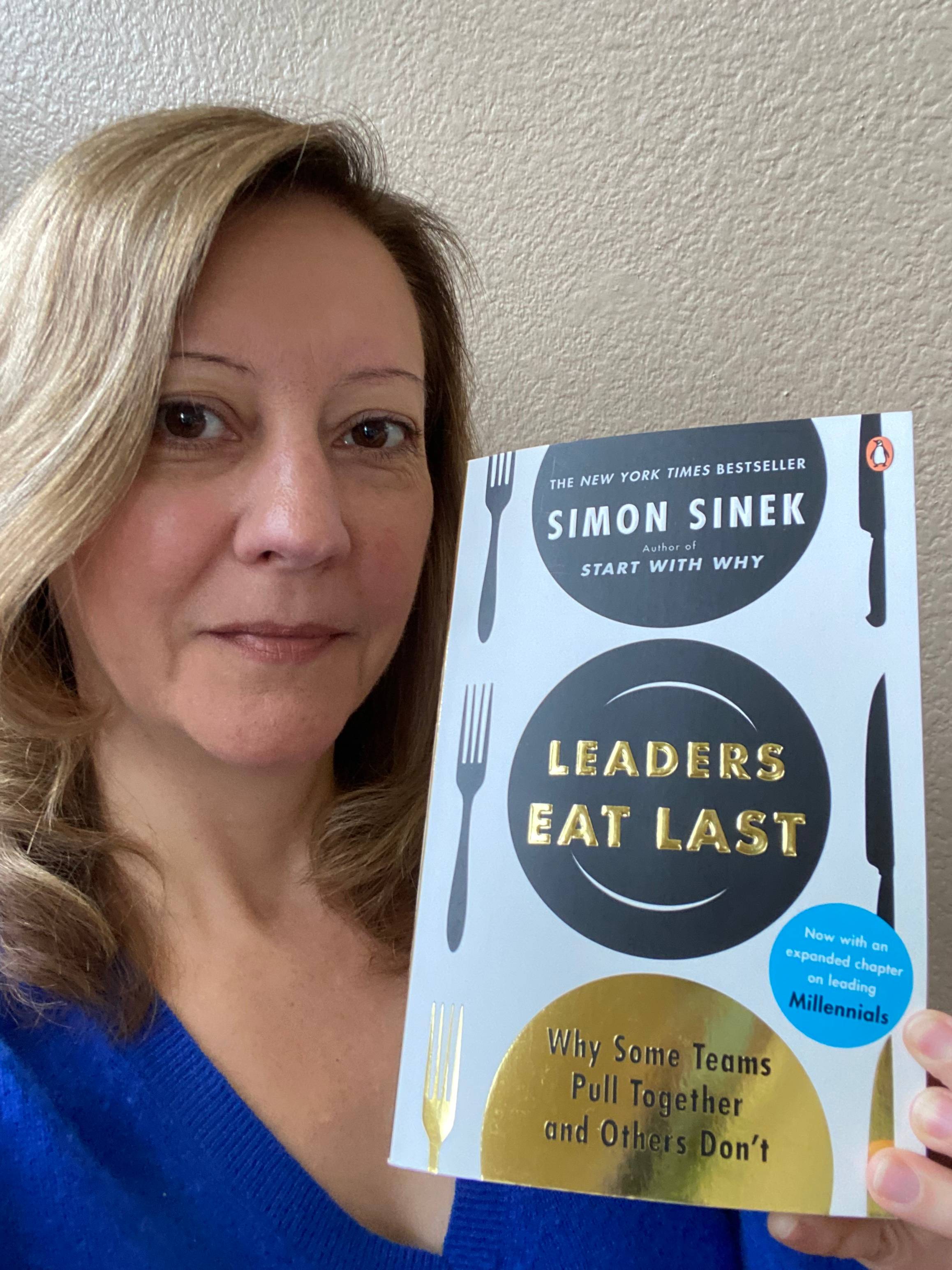 A photo of Stephanie holding the book "Leaders Eat Last" by Simon Sinek 