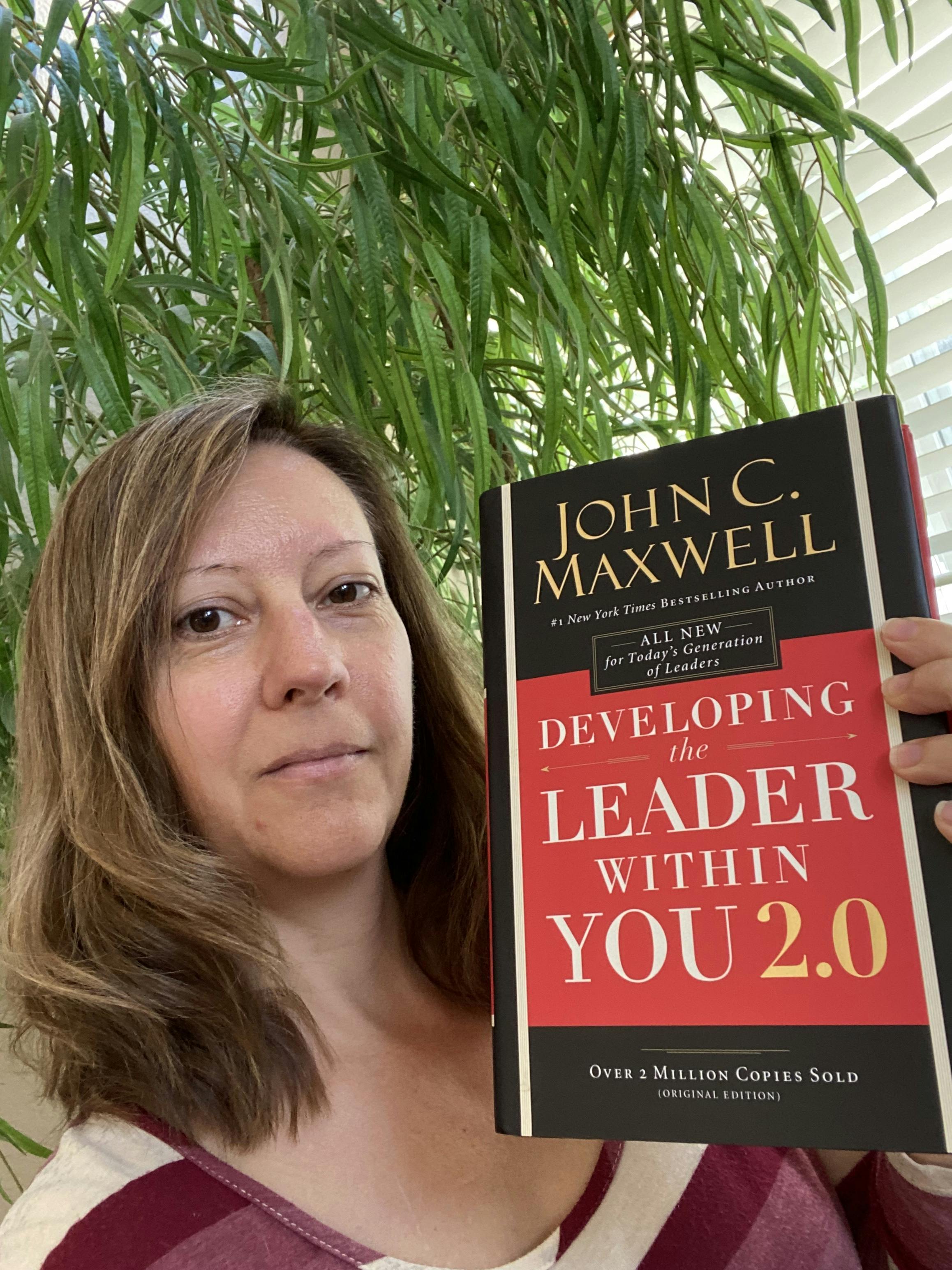 Stephanie holding the book "Developing the Leaders Within You 2.0" by John C. Maxwell. 