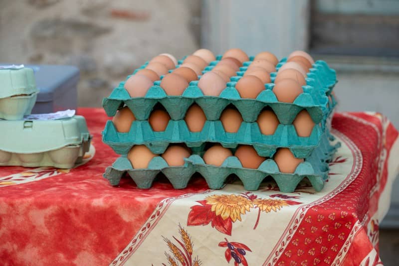 Stacked green cardboard egg cartons filled with brown eggs on a patterned tablecloth
