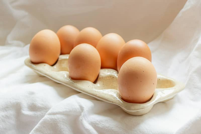 A group of brown eggs in a ceramic tray on white fabric