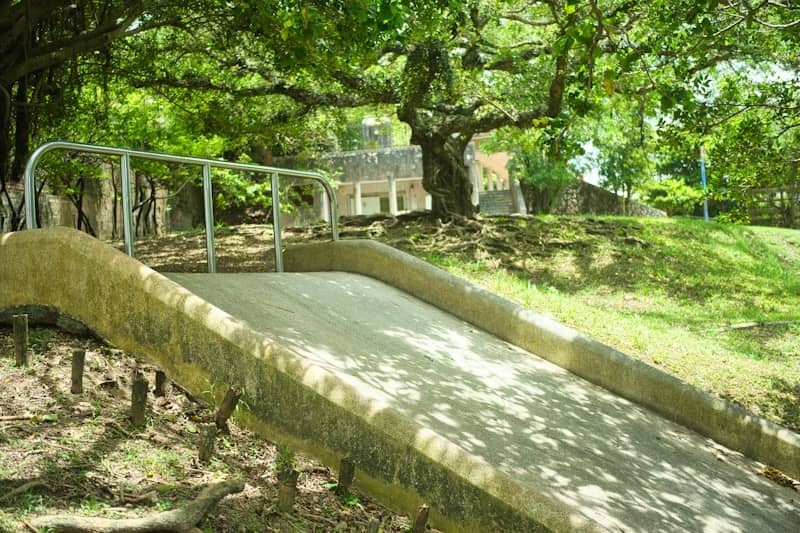 A concrete slide with metal railings in a green park.