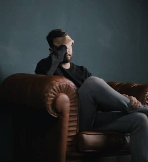 a man holds his head while sitting on a sofa