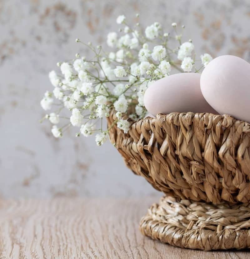 Eggs and flowers rest in a woven basket.