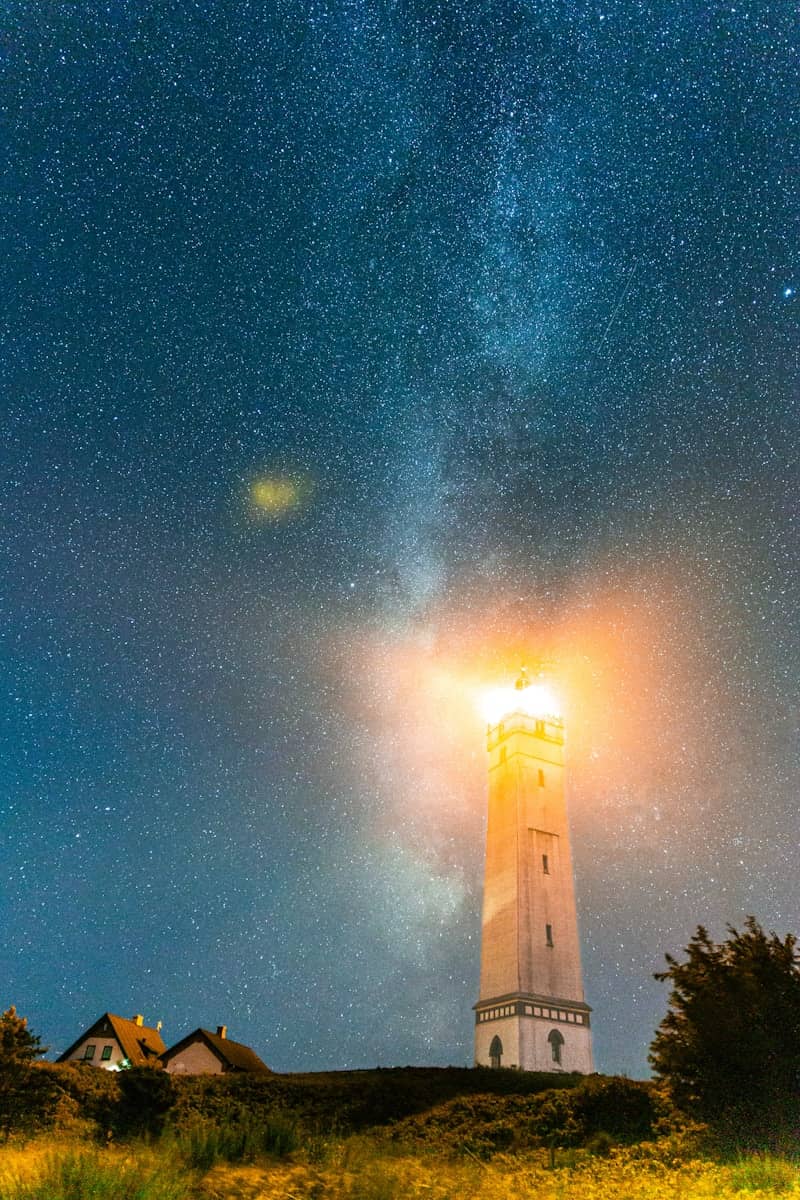 A lighthouse on a hill under a night sky