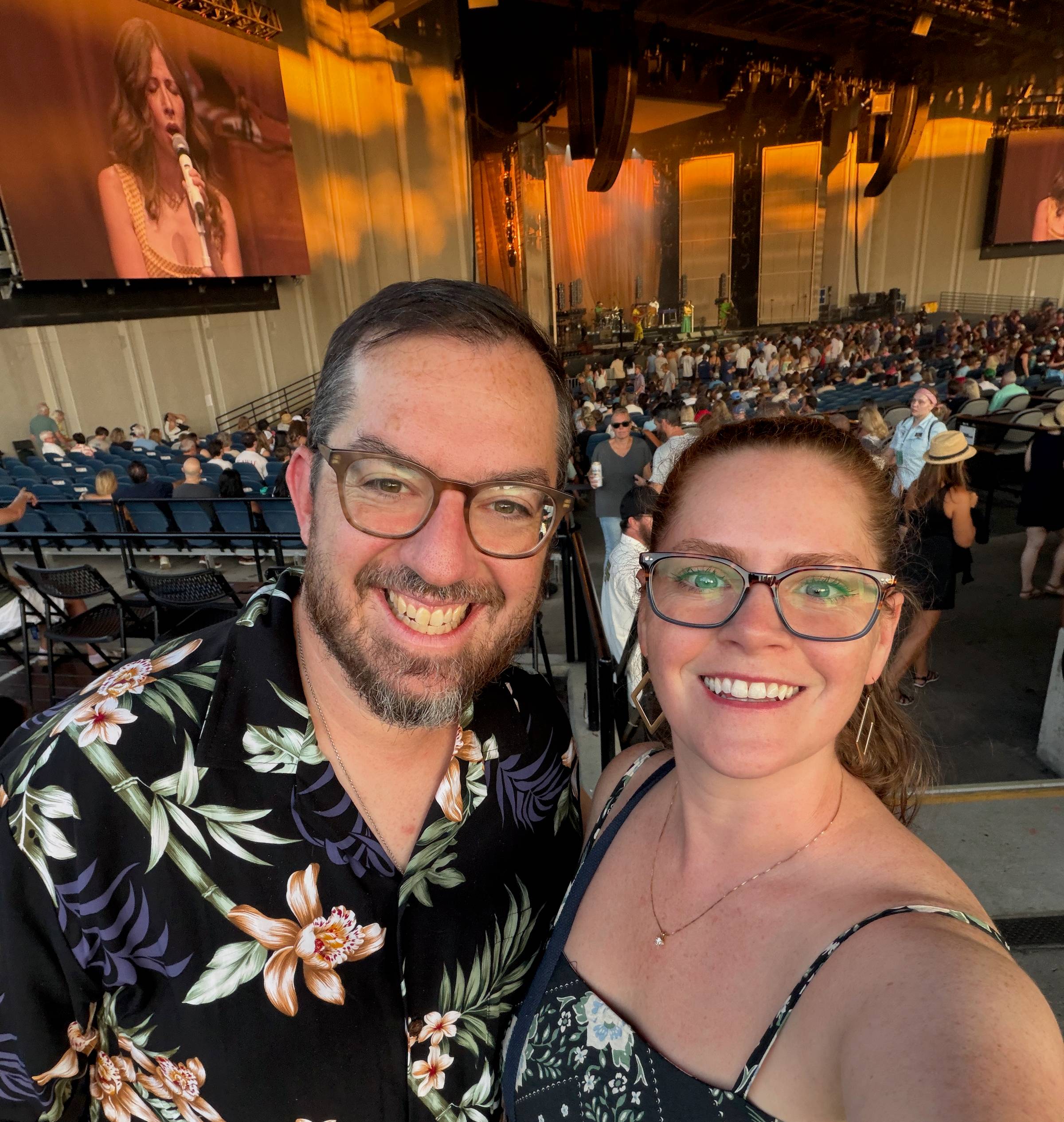 Natalie (right) and her husband (left) take a selfie in front of a concert stage.