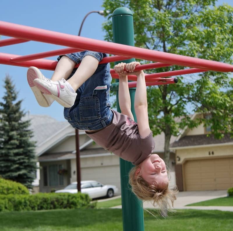 Young child hangs upside down on playground monkey bars
