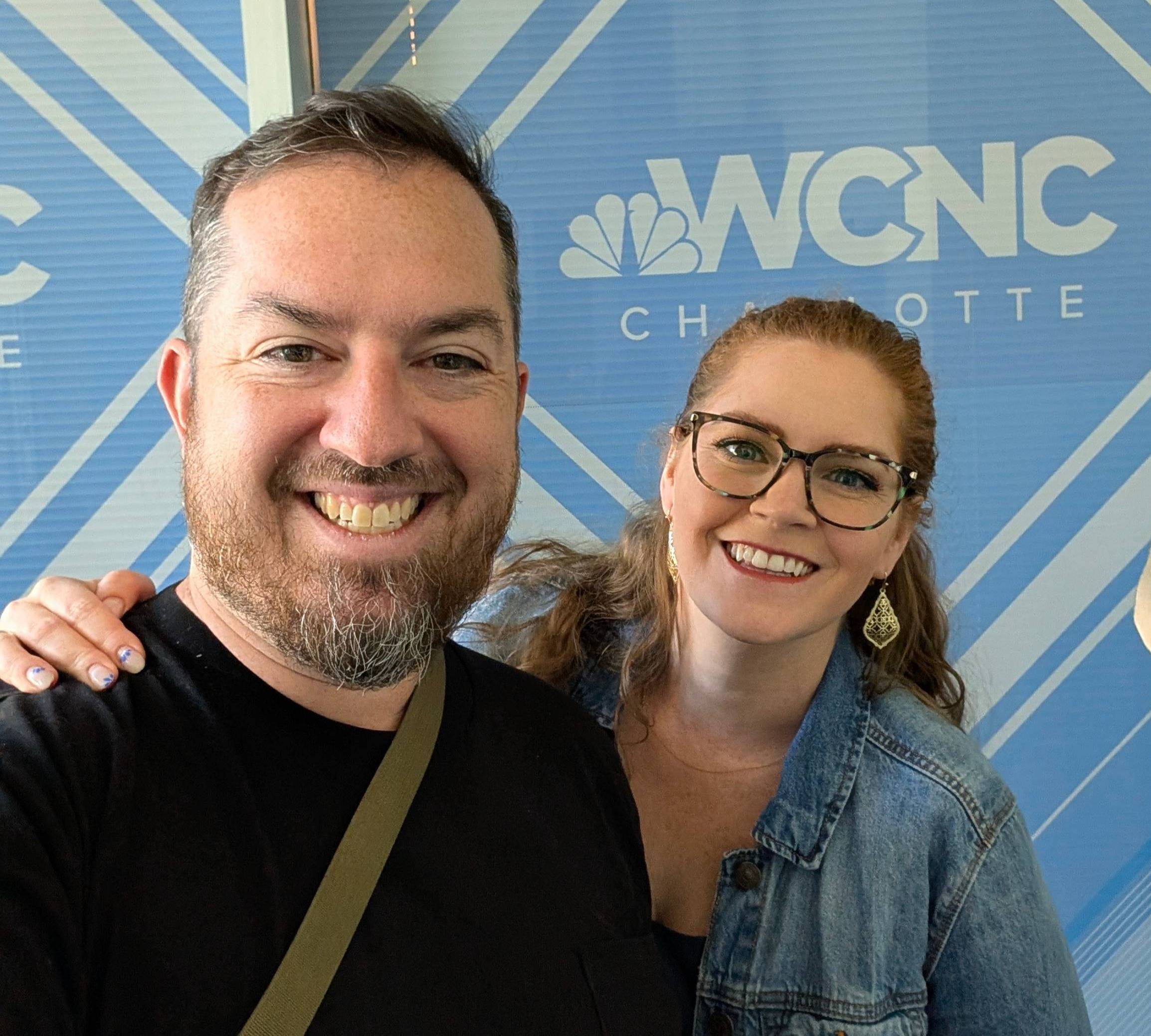 Natalie and her husband Mike take a selfie in front of a sign that says WCNC Charlotte
