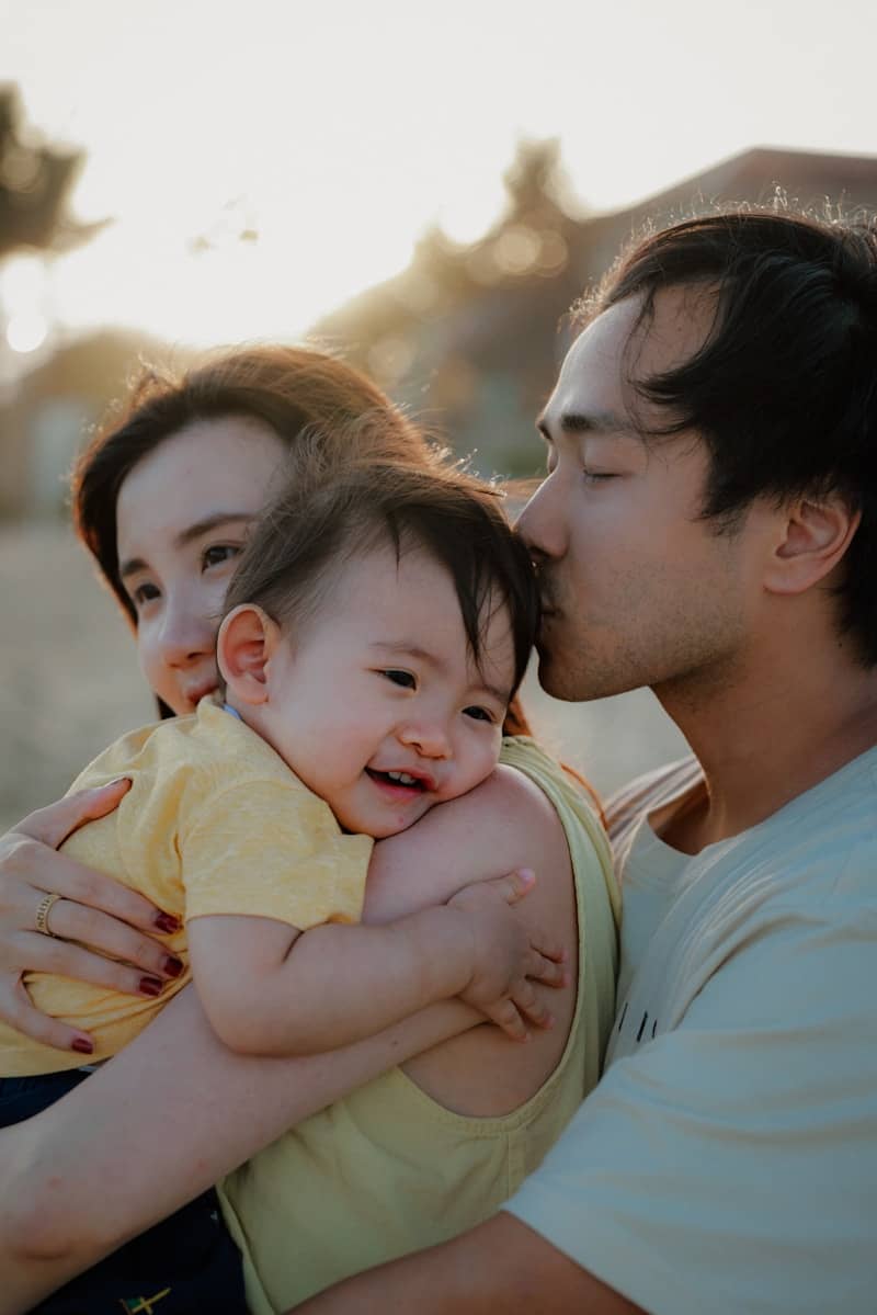 A father kisses his happy baby held by mother
