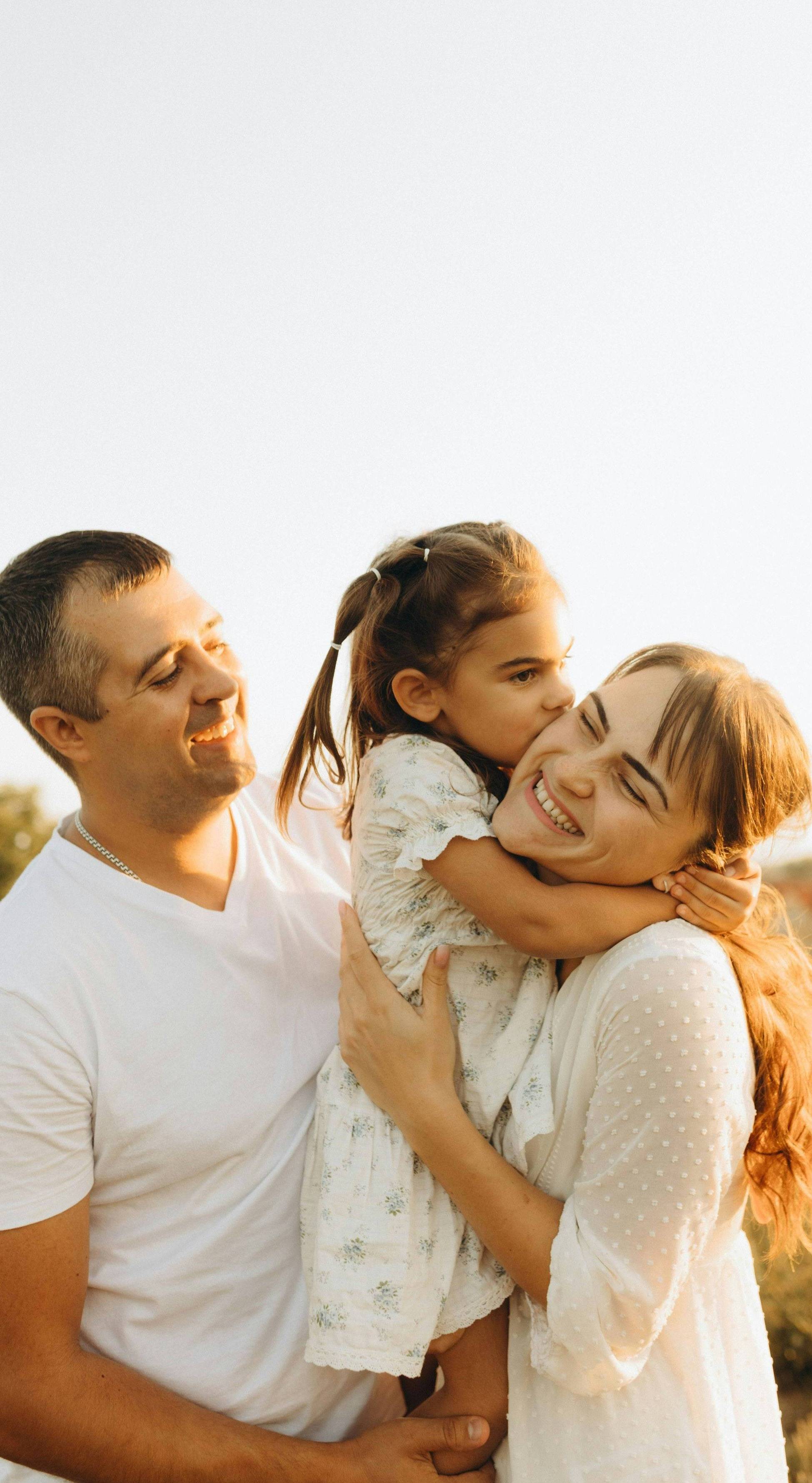 A father kisses his happy baby held by mother
