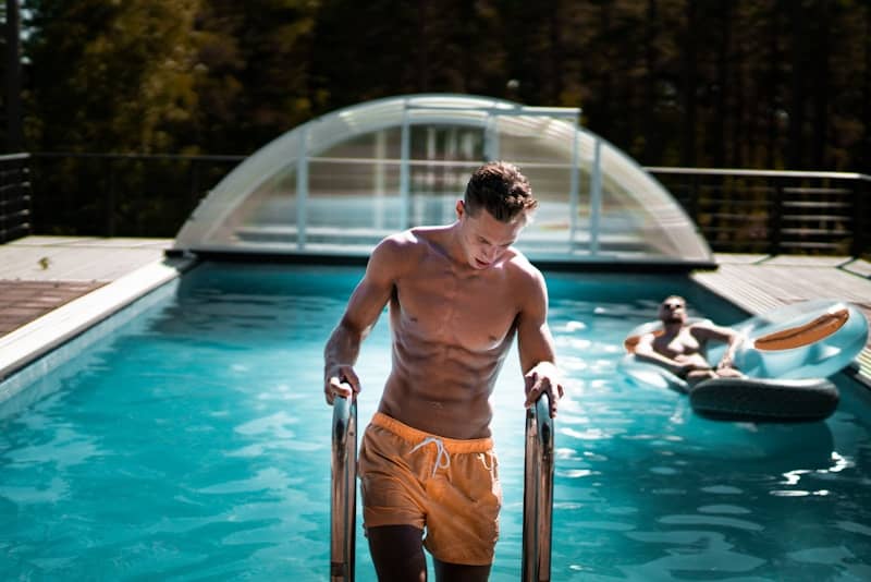 A man with a six pack walks out of a pool.