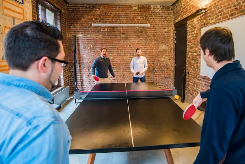 Four men playing table tennis in a brick-lined room.