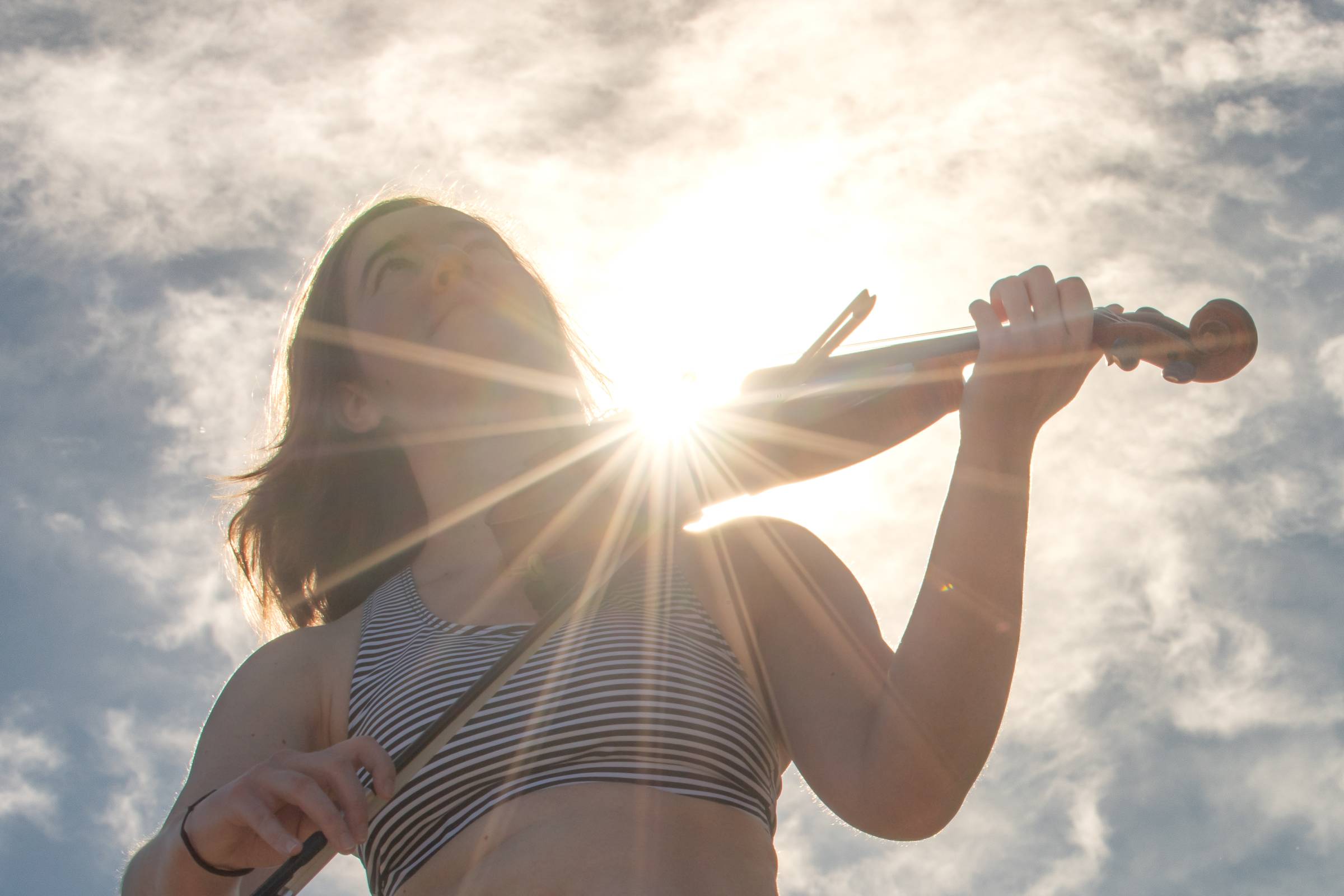 Hannah plays her fiddle outside with a sunlit background