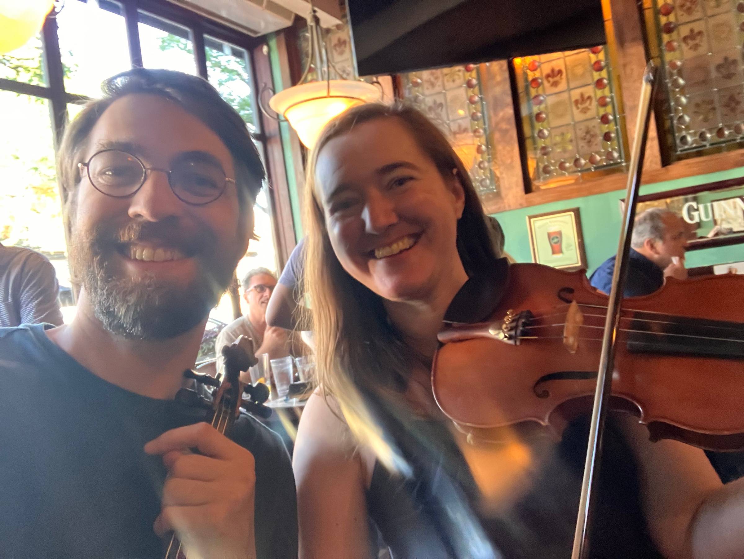 Two fiddlers smiling at the camera during an Irish traditional music session in southeast Michigan