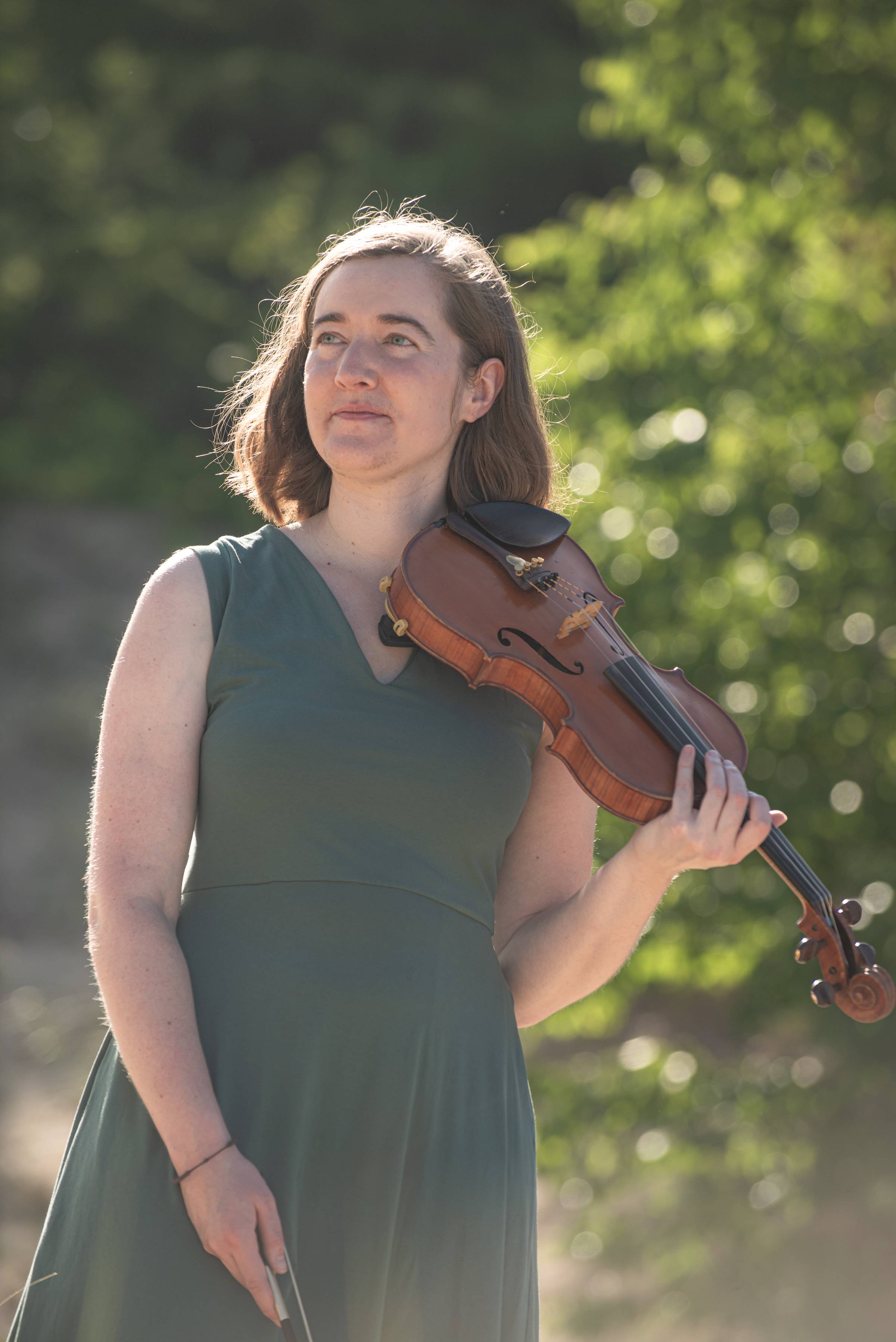 A girl in a green dress looks thoughtfully into the air while holding her fiddle