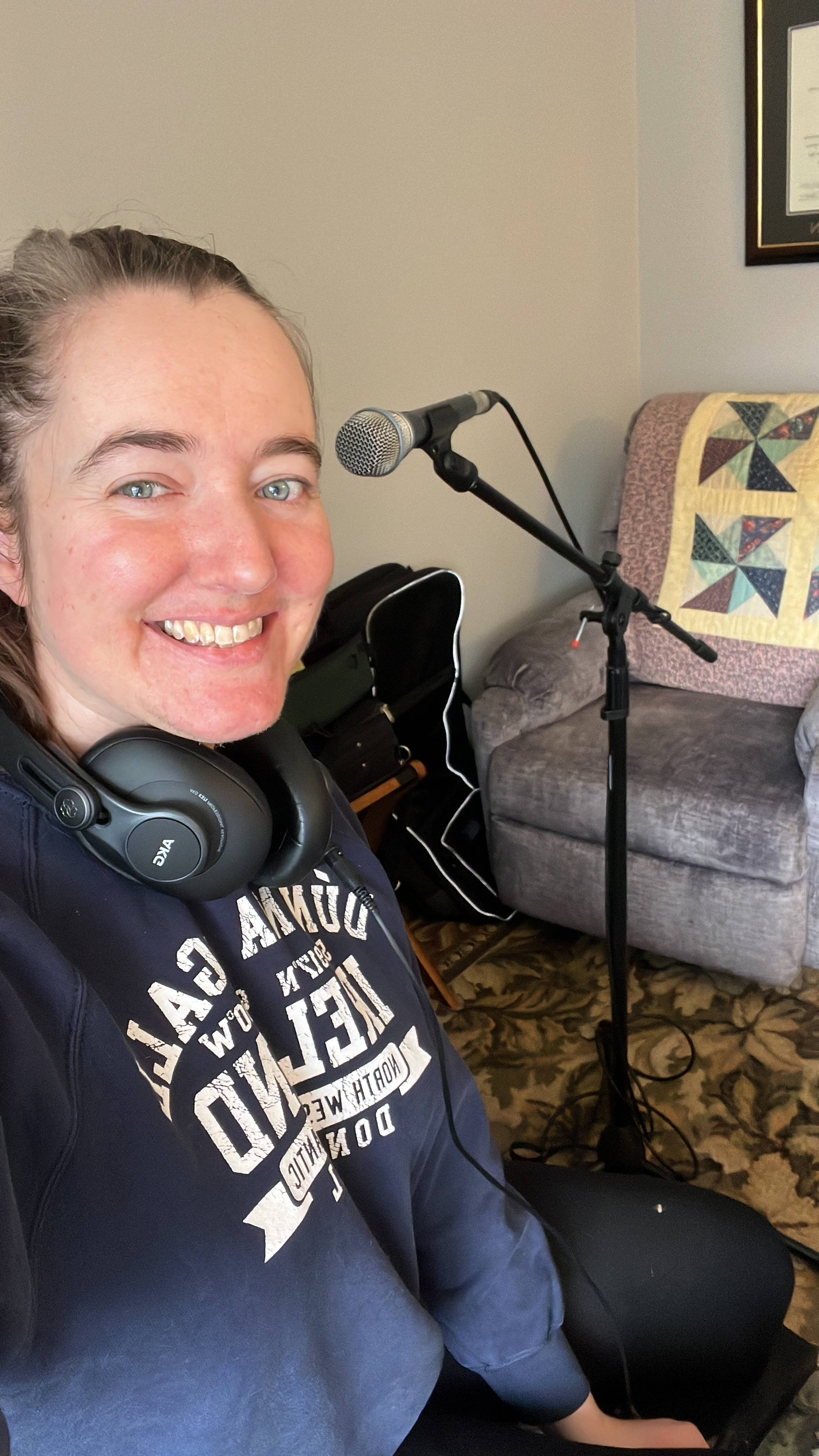 A girl with headphones and microphone smiling at the camera mid practice session
