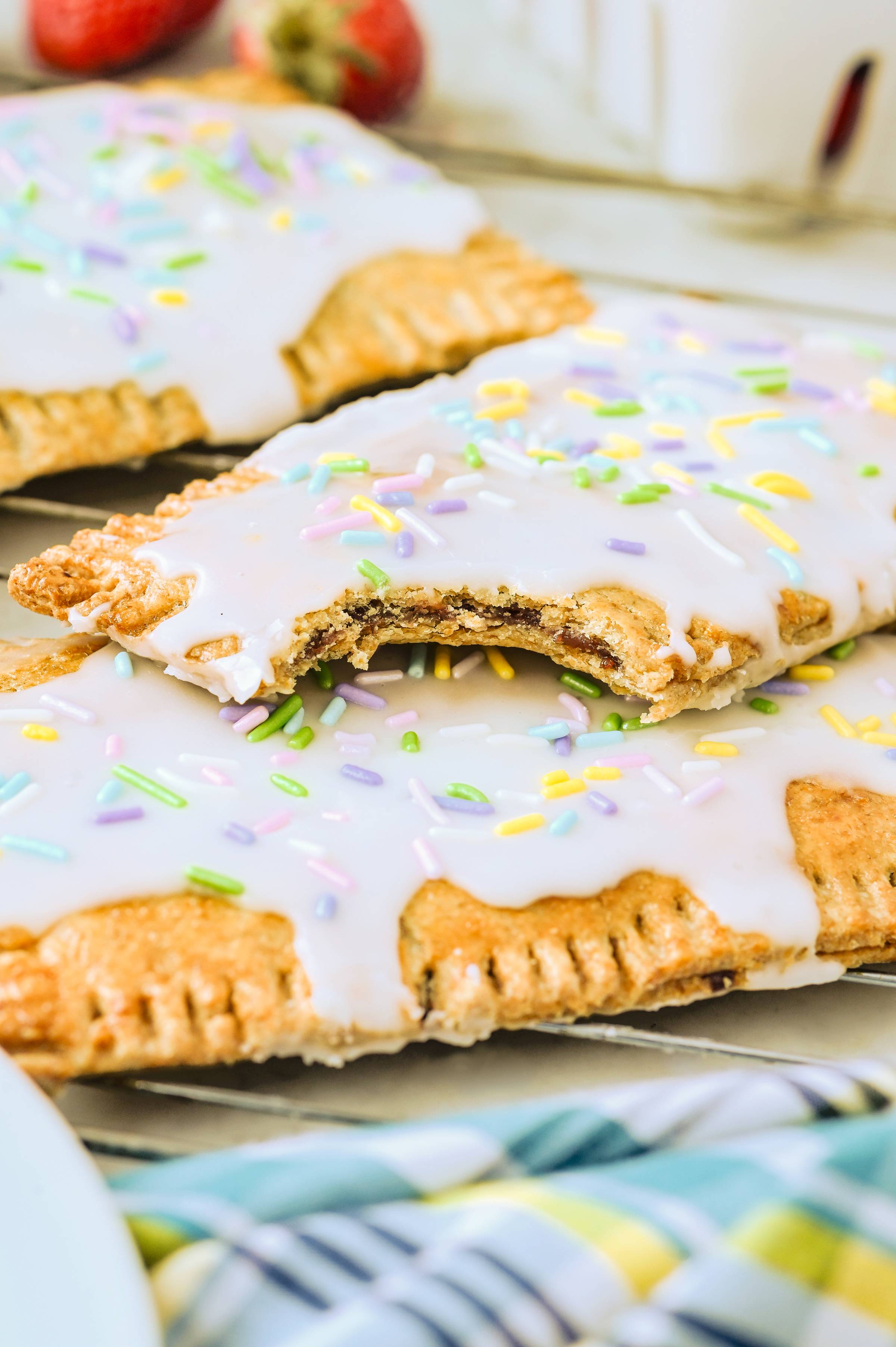 Homemade sourdough pop tarts with icing and colorful sprinkles, with one broken open to show the jam filling.