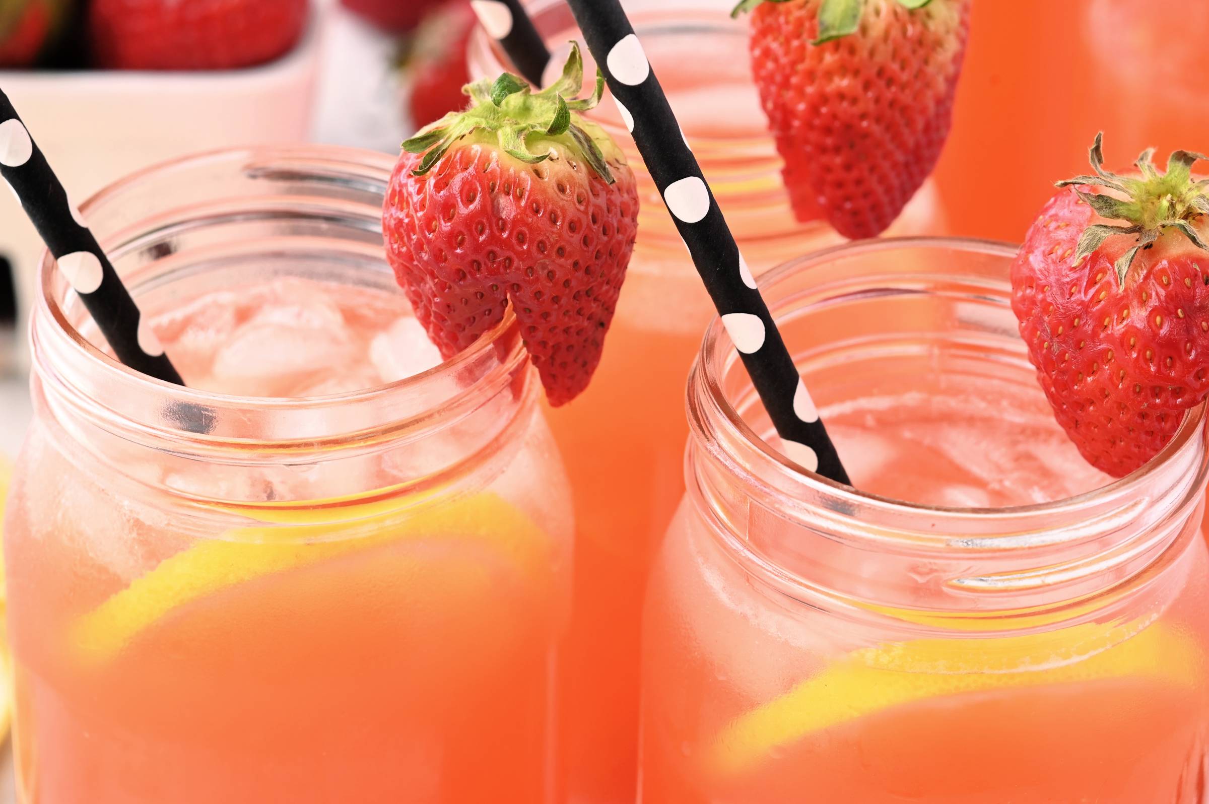 Mason jars of lacto fermented strawberry lemonade with lemon slices, ice, strawberries, and striped straws.