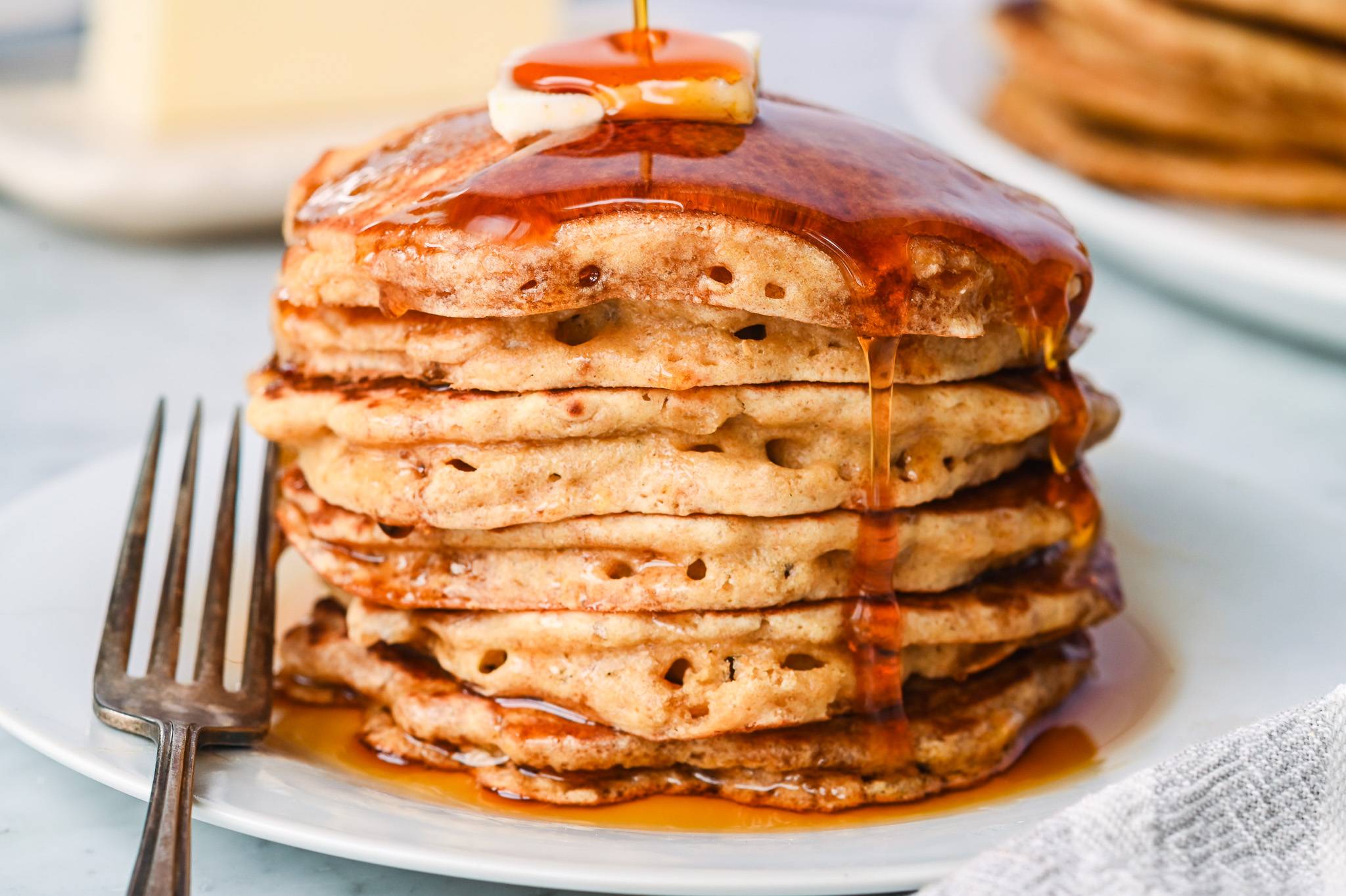 Stack of whole wheat pancakes made with fresh milled flour, topped with butter and maple syrup on a white plate.
