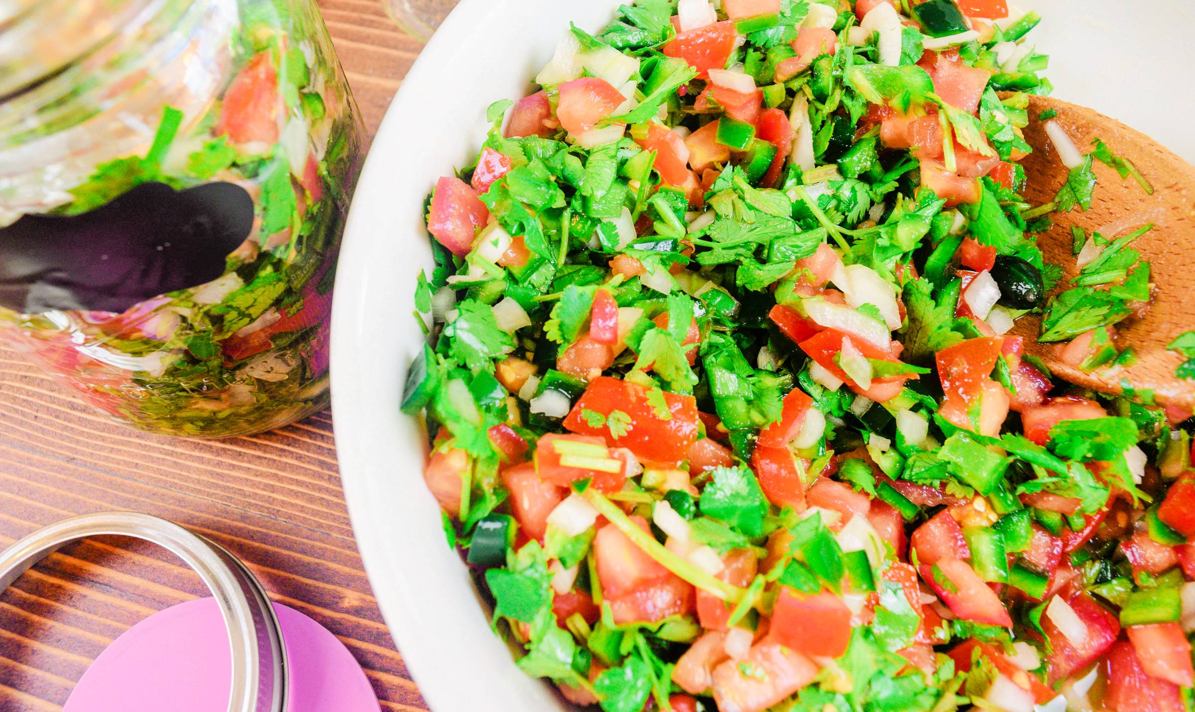 Fermented pico de gallo salsa with tomatoes, onion, jalapeños, and cilantro in a white bowl beside a glass jar.