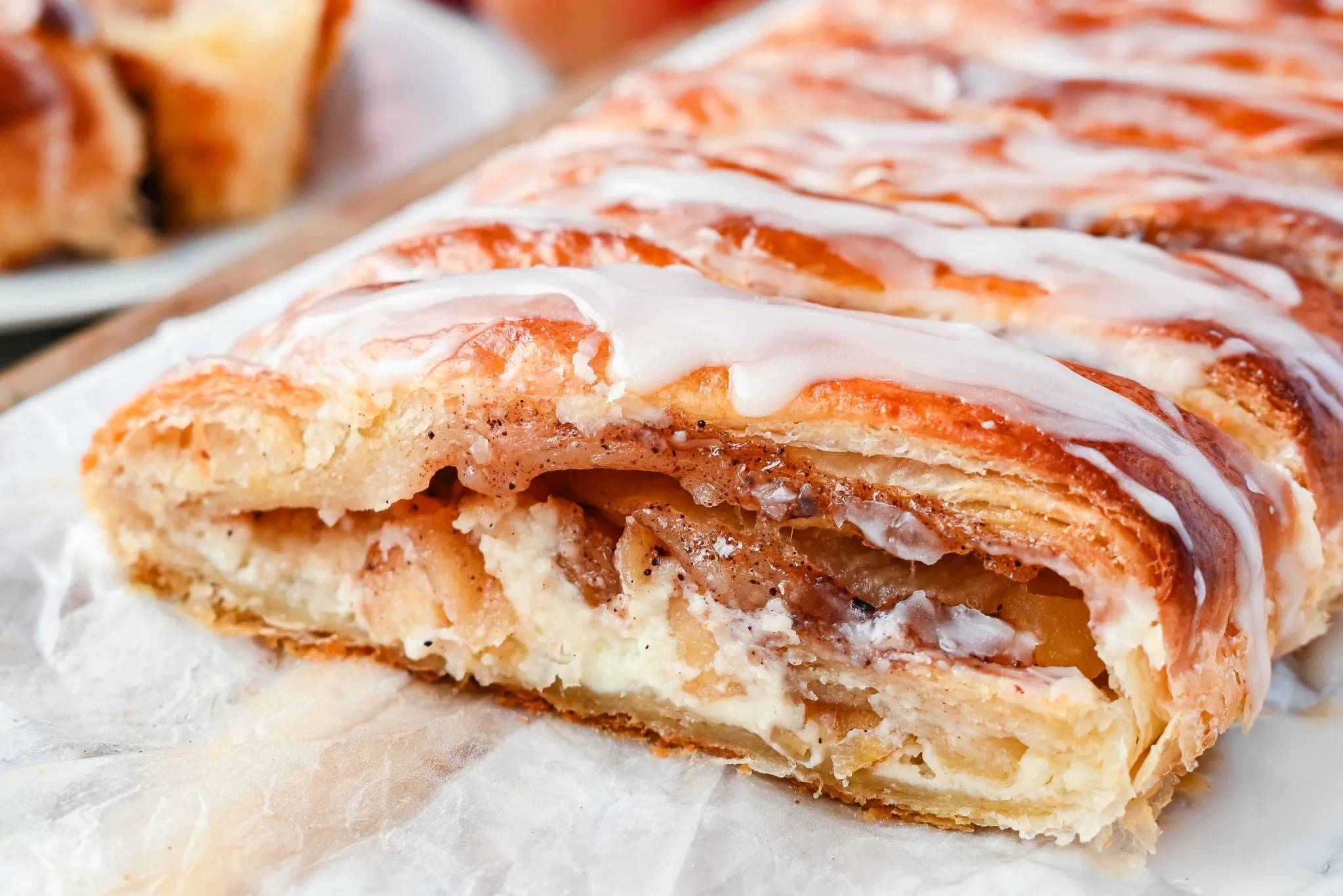 Close-up cross section of braided apple cream cheese puff pastry Danish revealing layers of flaky pastry, sweet cinnamon apples, and smooth cream cheese filling.