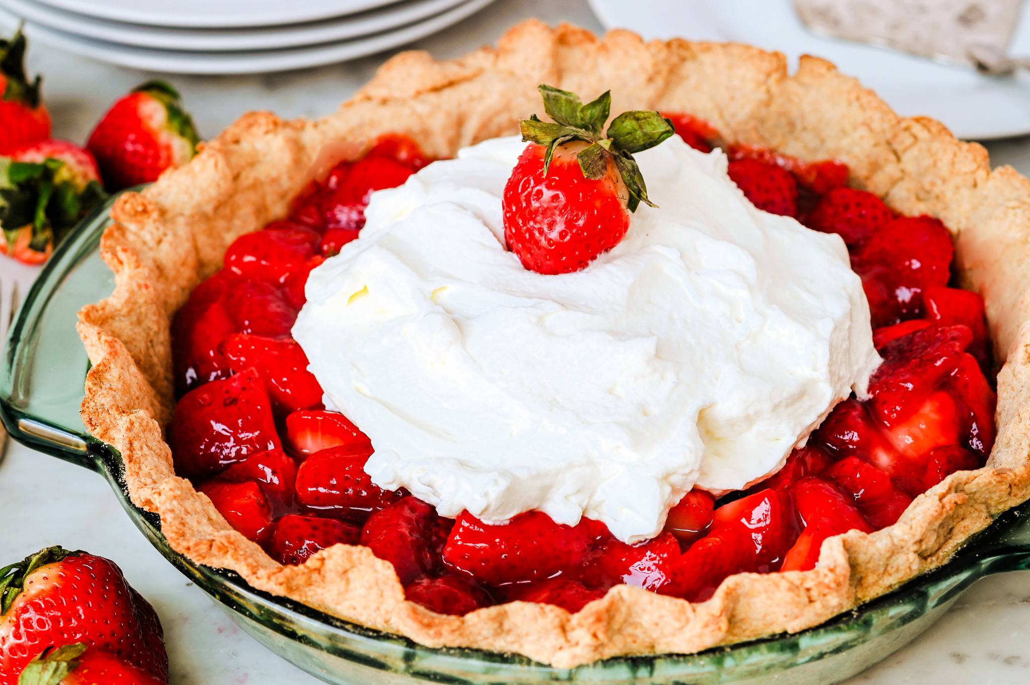 Homemade strawberry pie with fresh strawberry filling, whipped cream, and a whole strawberry on top.