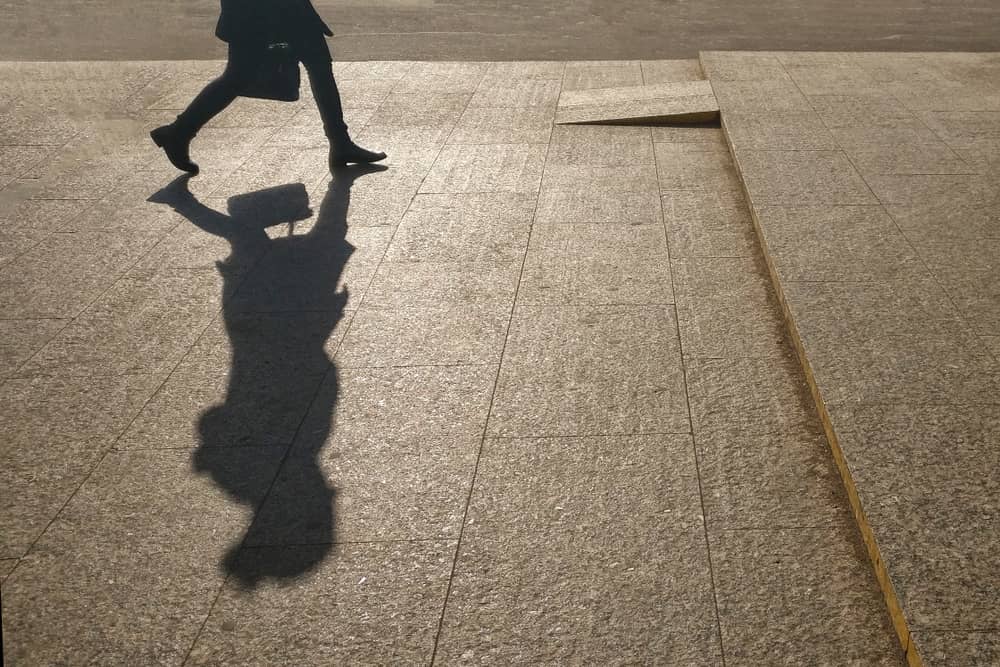 The silhouette of a person is walking from the left side of the image to the right side, with their shadow prominently present in the image as well.