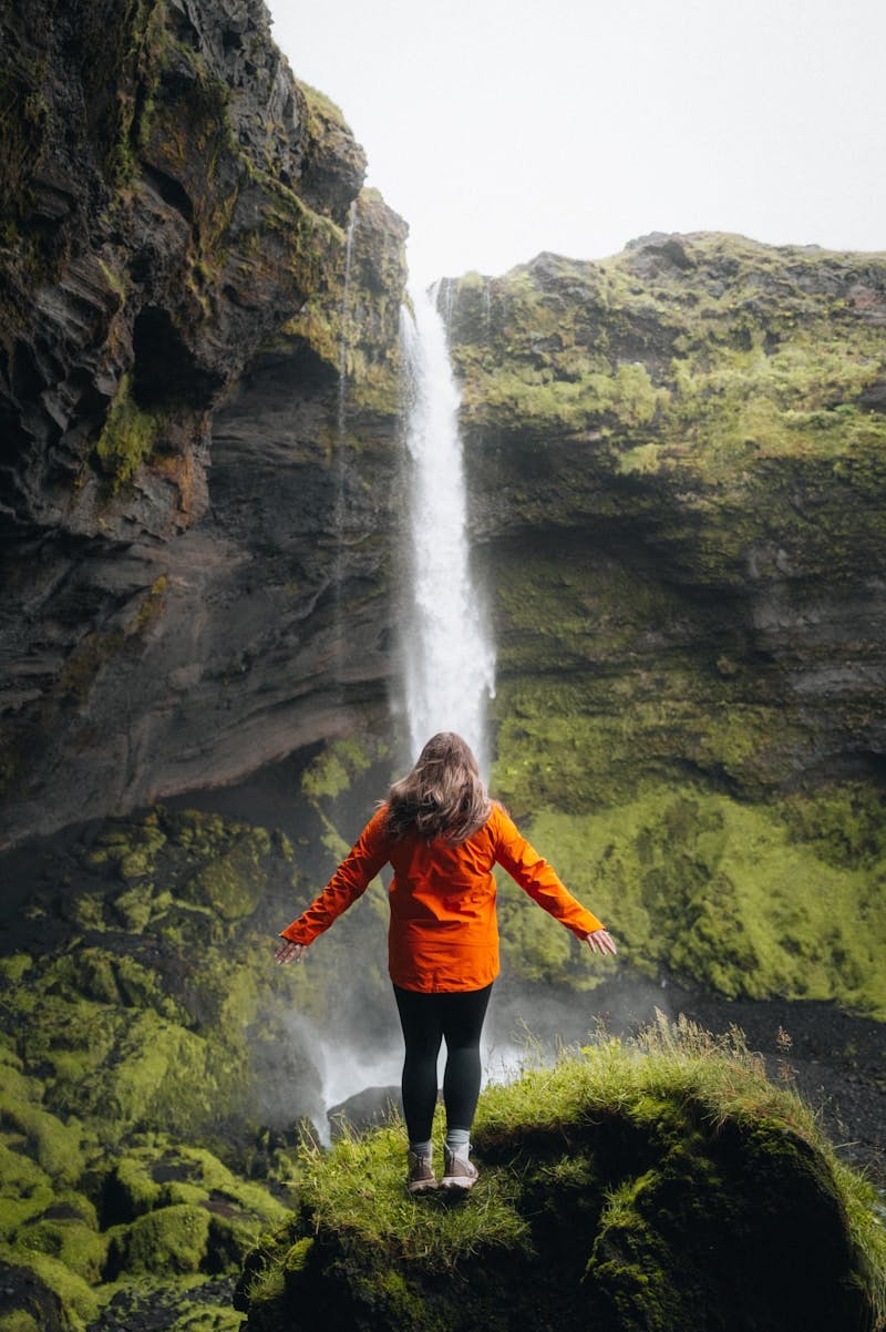 A woman in an orange jacket standing in front of a waterfall