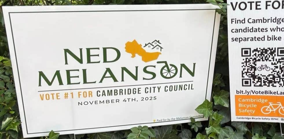 A "Ned Melanson for Cambrige City Council" sign sits next to another yard sign atop some ivy
