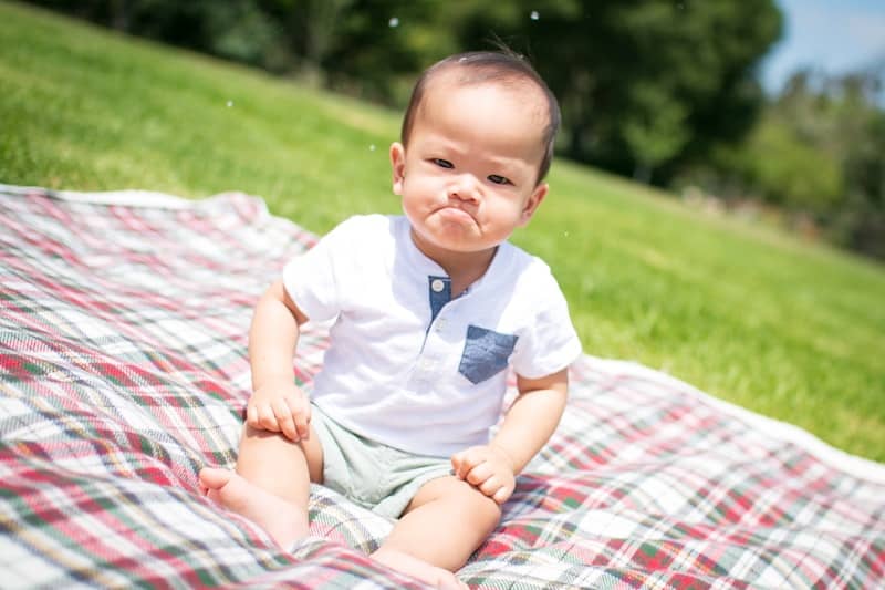 grumpy baby in white clothes on blanket