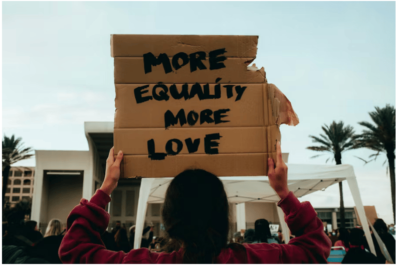woman holds up cardboard sign over her head reading: more equality more love