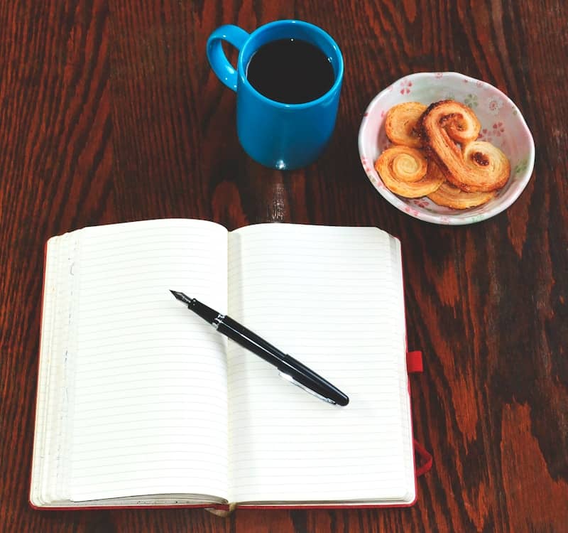 red ceramic mug beside black click pen on white paper