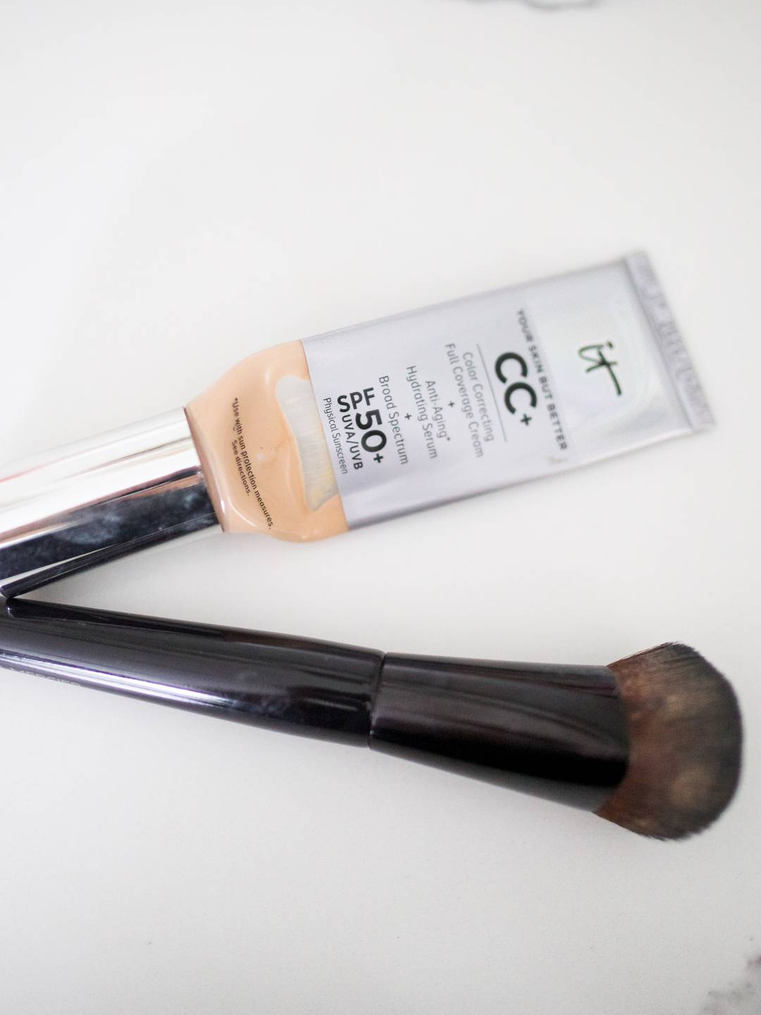 Tube of IT Cosmetics CC+ Cream with SPF 50 and a foundation brush on a white background.