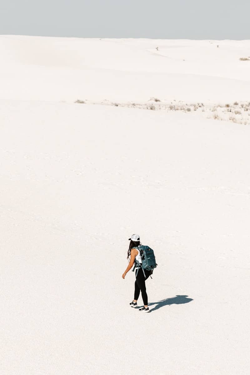 Woman with backpack walking across vast white desert landscape.