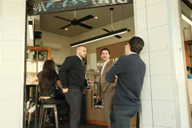 Three men talking and laughing outside a cafe entrance.