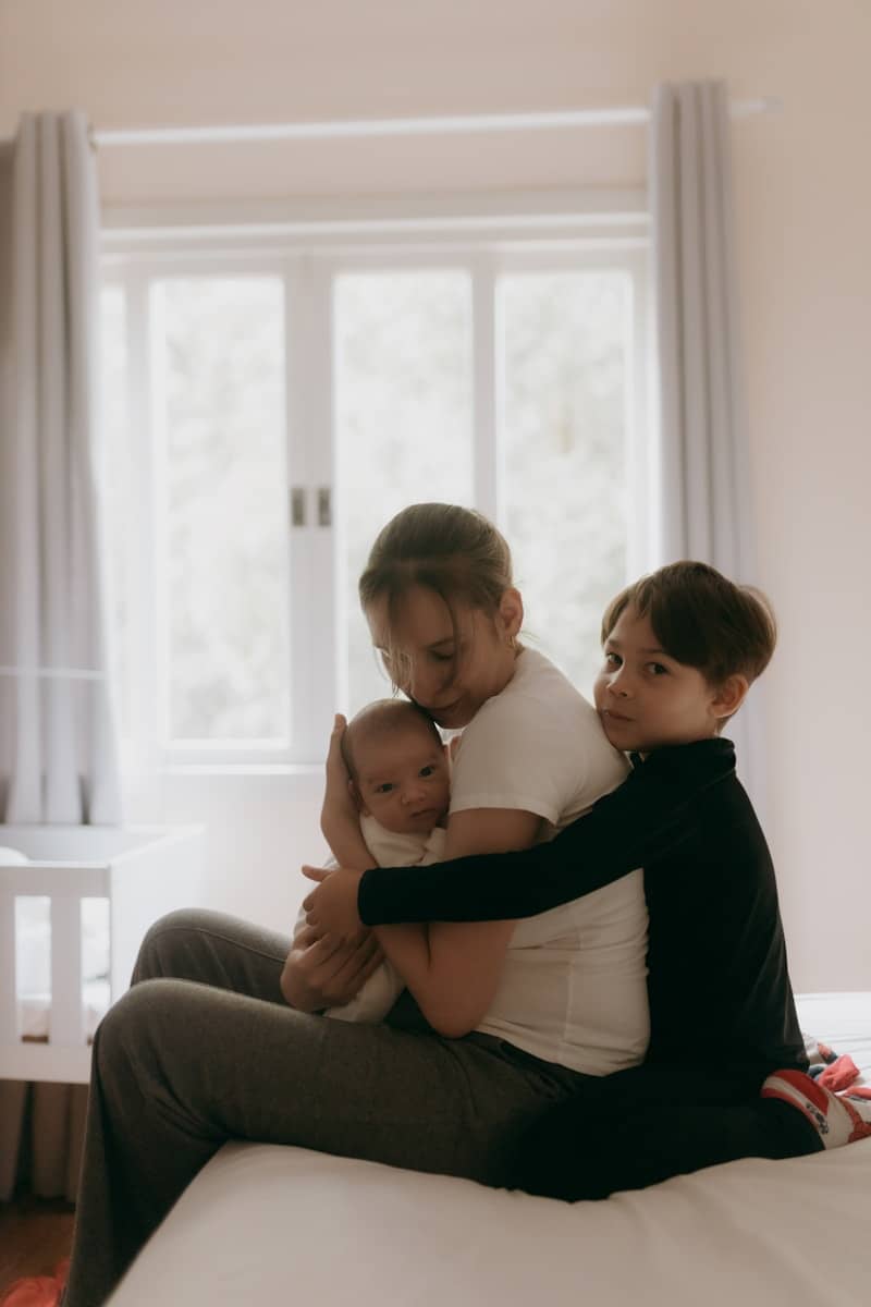 A mother and her children embrace on the bed.