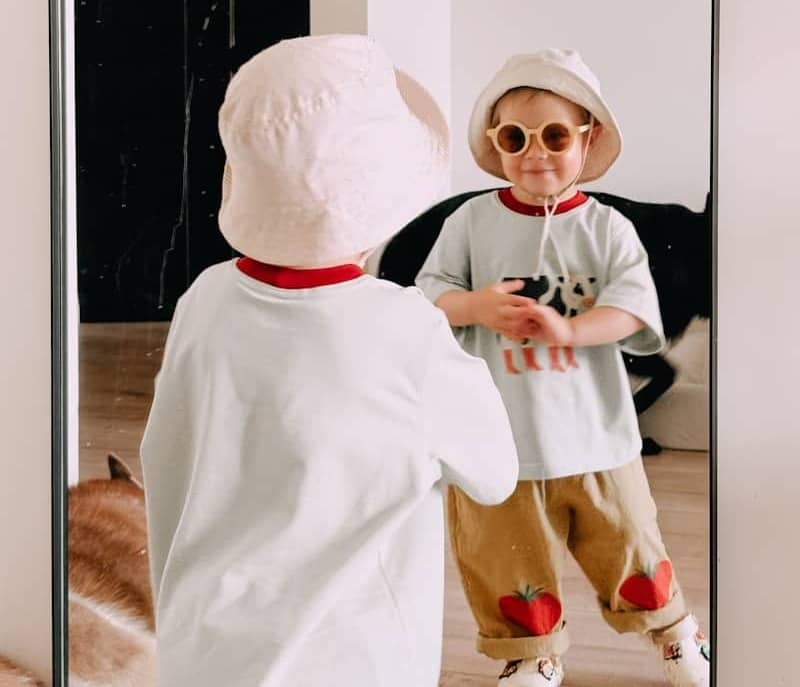 A cute toddler looks at their reflection in the mirror.