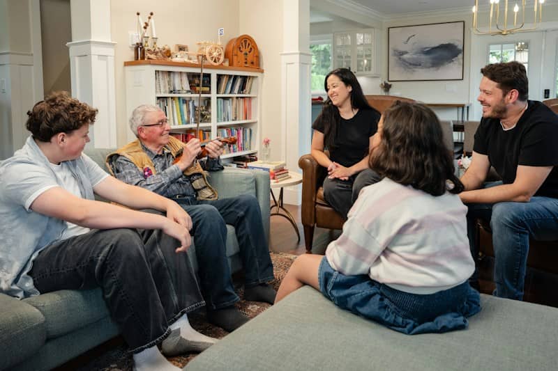 A family in a living room with an older man holding a violin