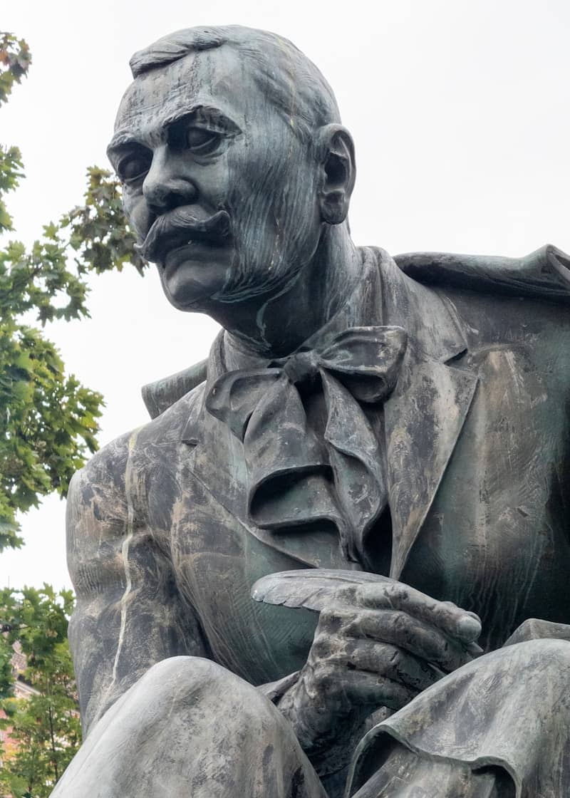 A weathered bronze statue of a man with a mustache.