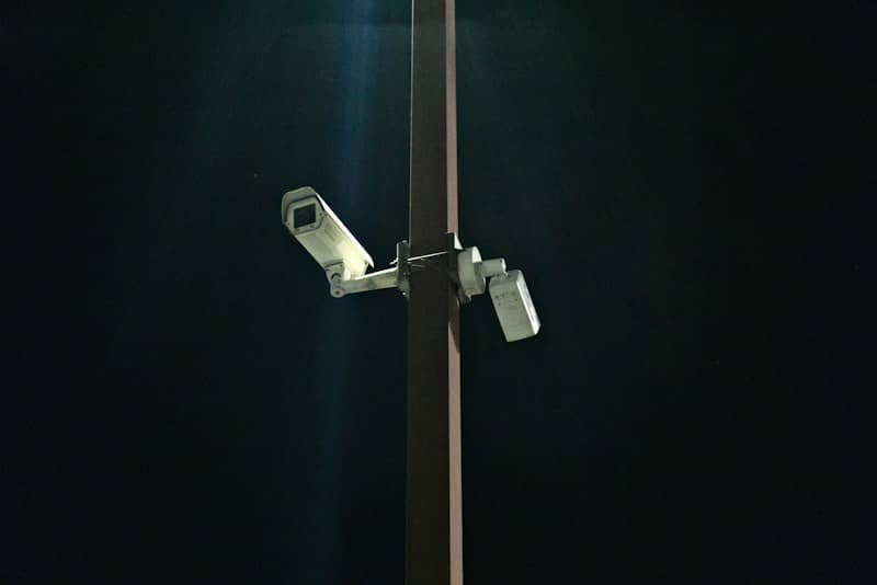 Two security cameras mounted on a tall pole against a dark night sky