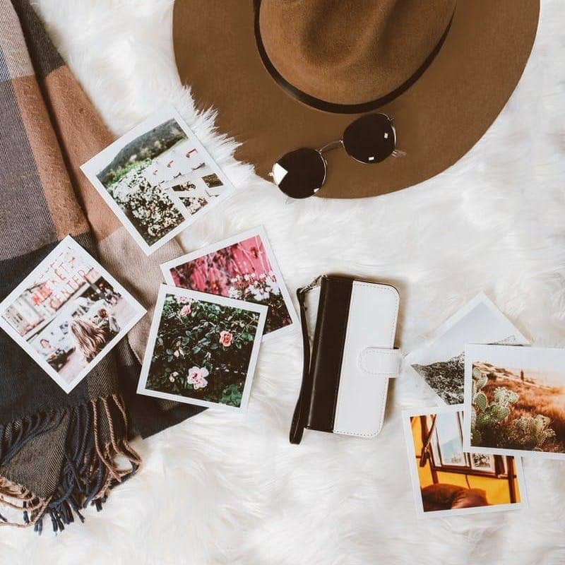 gold-colored framed sunglasses on brown hat beside white and black leather wristlet surrounded by photos on white and gray floral textile