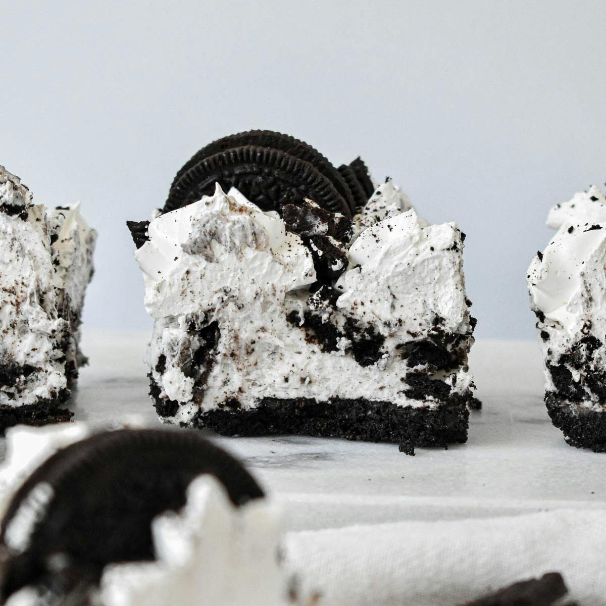 Slice of Oreo no bake dessert with an Oreo crust and black and white filling topped with whipped frosting and Oreo garnish